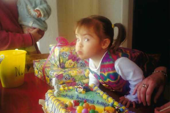 Child blowing out candles on a birthday cake with presents in the background